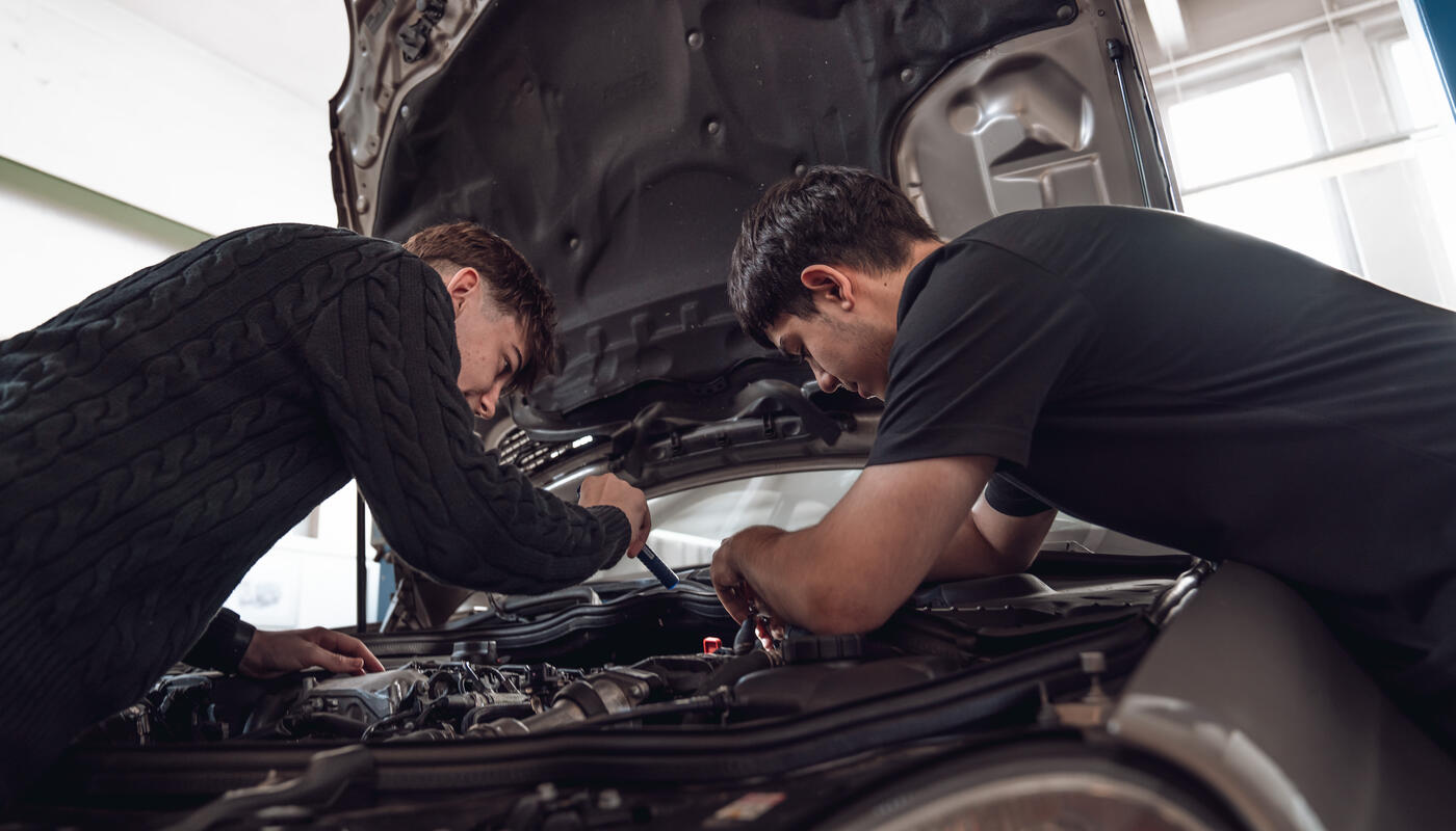 Lehrlinge bei Merbag schrauben unter der Motorhaube